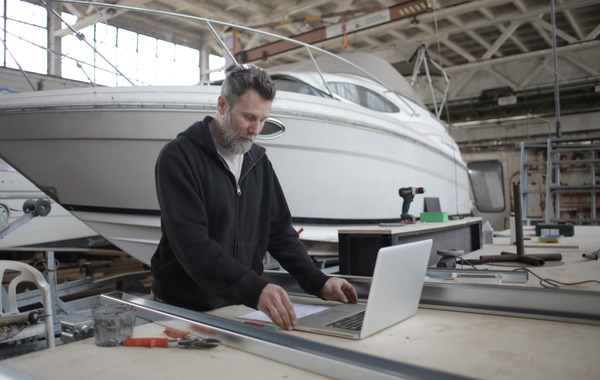 A man using a laptop with a white boat behind him